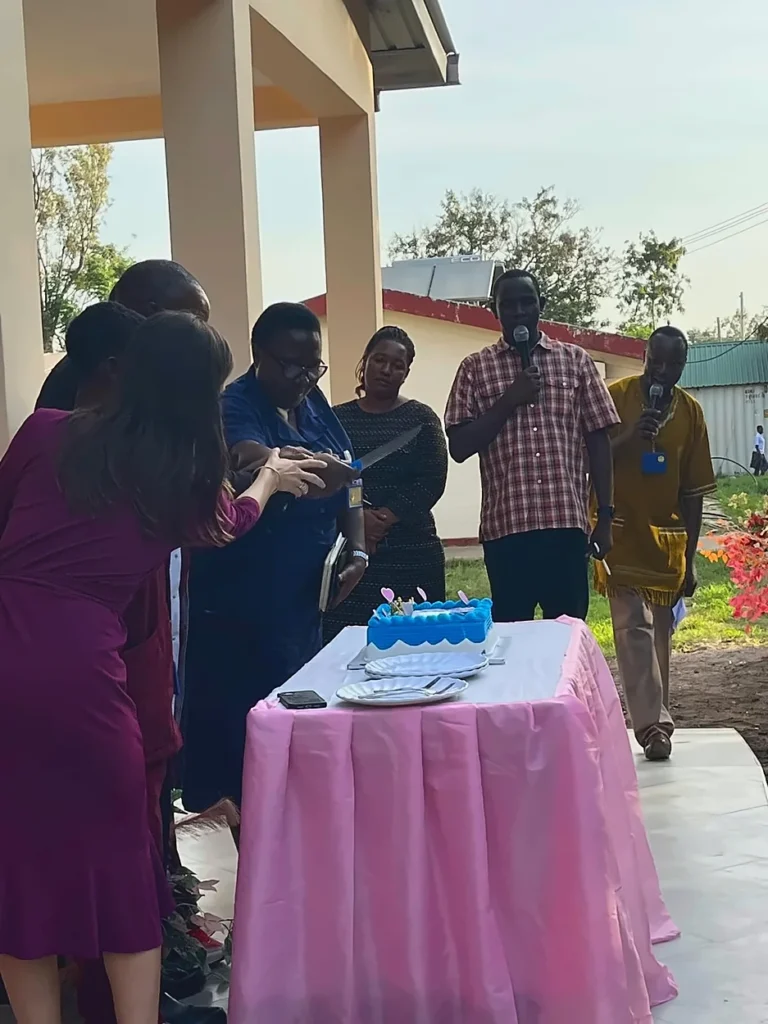 A group of people cutting a cake during the Shirati Opening ceremony outside.